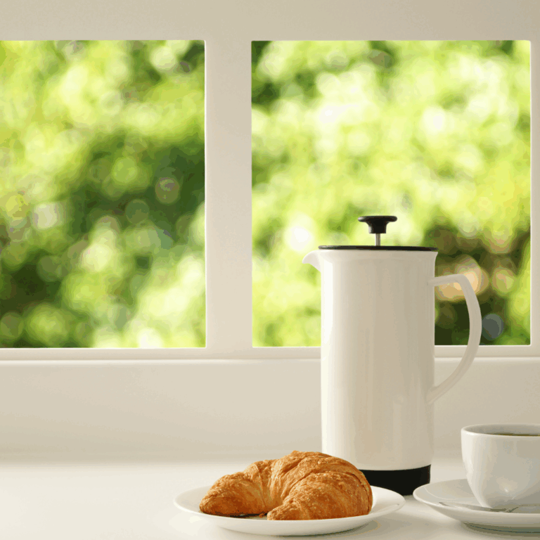 White French press coffee maker on a sunny balcony table with blurred greenery in the background