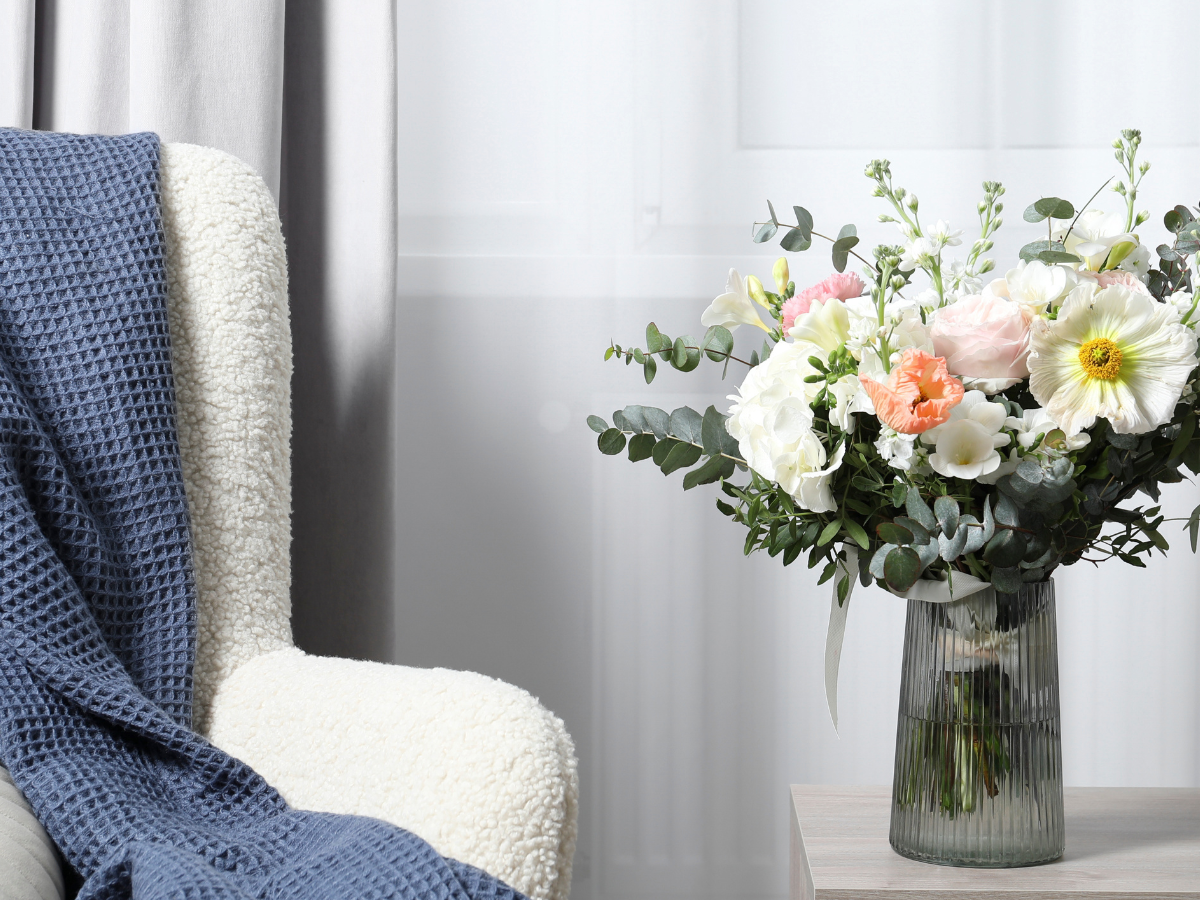 Soft pastel floral arrangement in glass vase beside cozy armchair