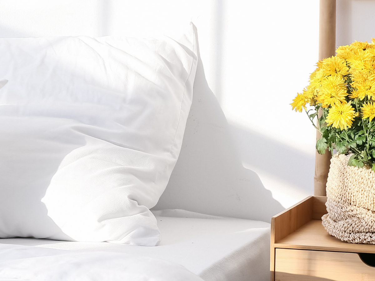 Three terracotta pots with artificial flowers in yellow, white, and orange, displayed inside a rustic wooden crate on a white wall.