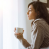 Woman in cozy sweater holding a mug while looking out the window.