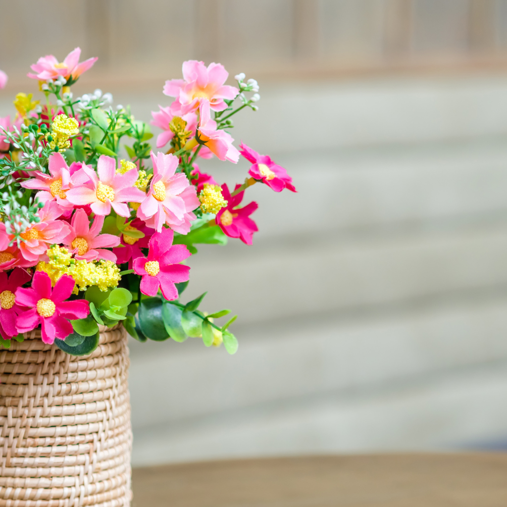Vibrant pink and yellow artificial flowers in a woven rattan basket