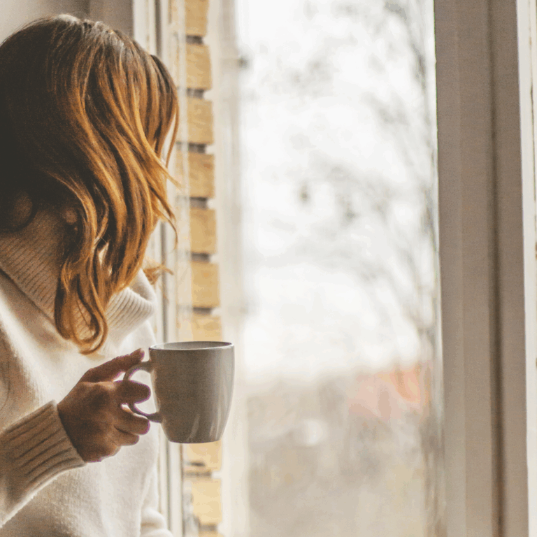 Woman in white sweater holding a mug by the window