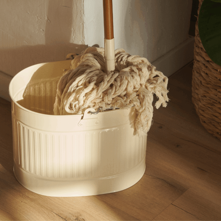 Traditional mop placed inside a beige cleaning bucket in a home corner setting.