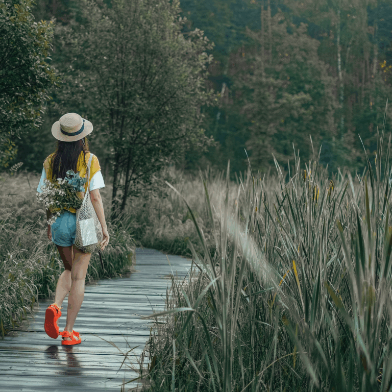 Woman walking on a wooden path surrounded by tall grass
