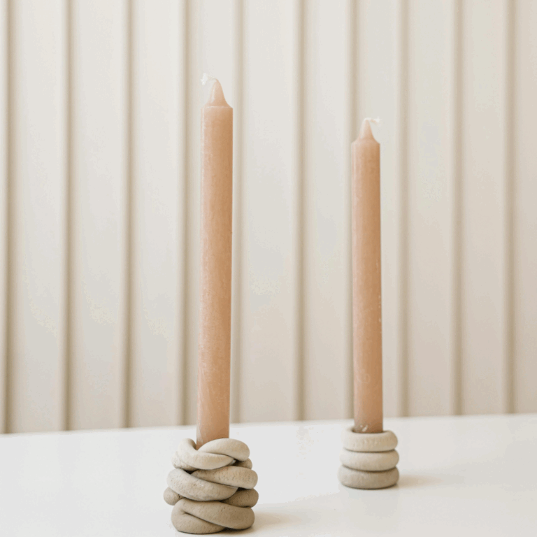 Minimalist taper candles in knotted ceramic holders on a white table with a neutral background