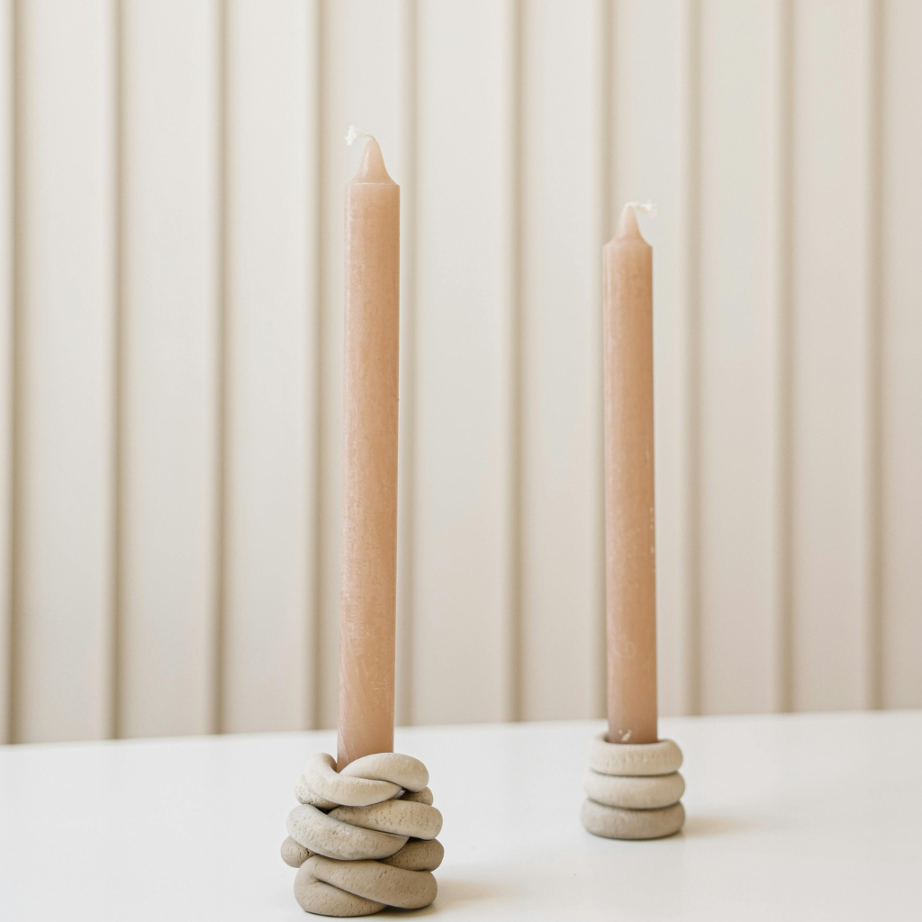 Minimalist taper candles in knotted ceramic holders on a white table with a neutral background