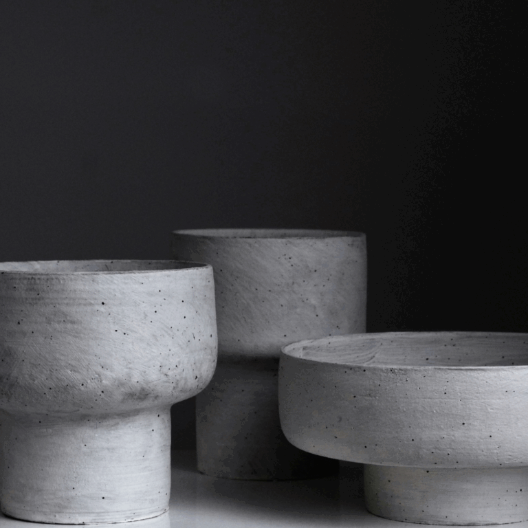Set of three sculptural gray concrete-style vessels in different shapes on a dark background
