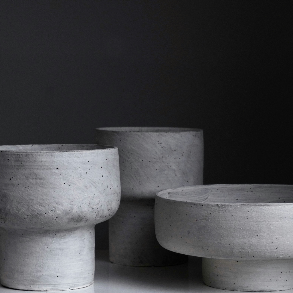 Set of three sculptural gray concrete-style vessels in different shapes on a dark background