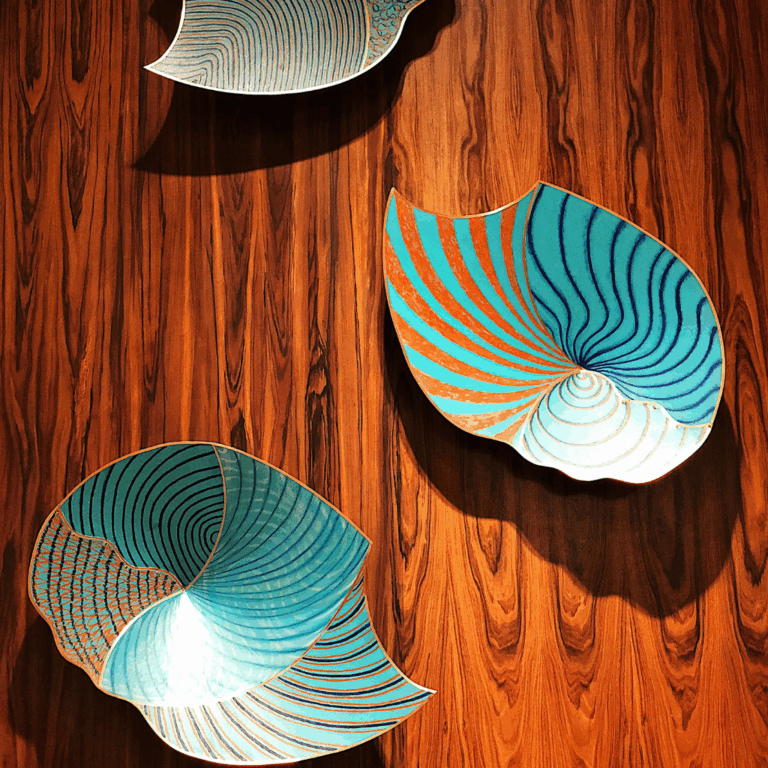 Three ceramic leaf trays in turquoise and copper tones mounted on a wooden wall