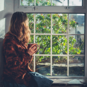 Woman in a cozy sweater holding a mug and looking out a sunny window