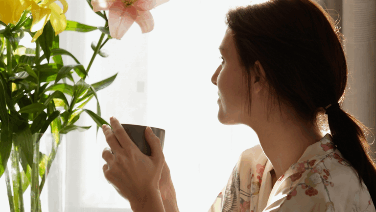Woman enjoying a quiet morning moment with a cup of coffee while admiring fresh flowers – from the blog "3 Mini Rituals You Can Create in Under 5 Minutes (Using Everyday Decor).