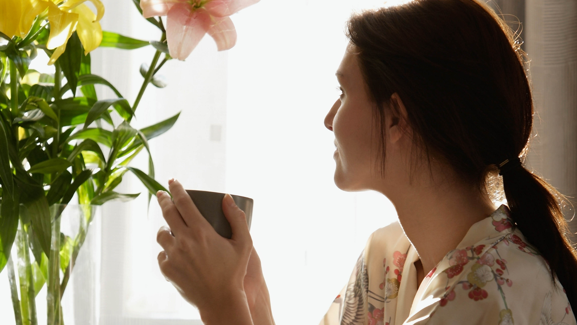 Woman enjoying a quiet morning moment with a cup of coffee while admiring fresh flowers – from the blog "3 Mini Rituals You Can Create in Under 5 Minutes (Using Everyday Decor).