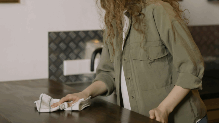 Person cleaning a wooden kitchen counter with a cloth to maintain a tidy and calming home environment