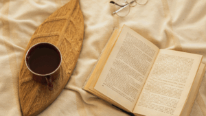 Cozy flat lay of a warm drink on a wooden tray next to an open book and glasses, symbolizing calming daily rituals at home