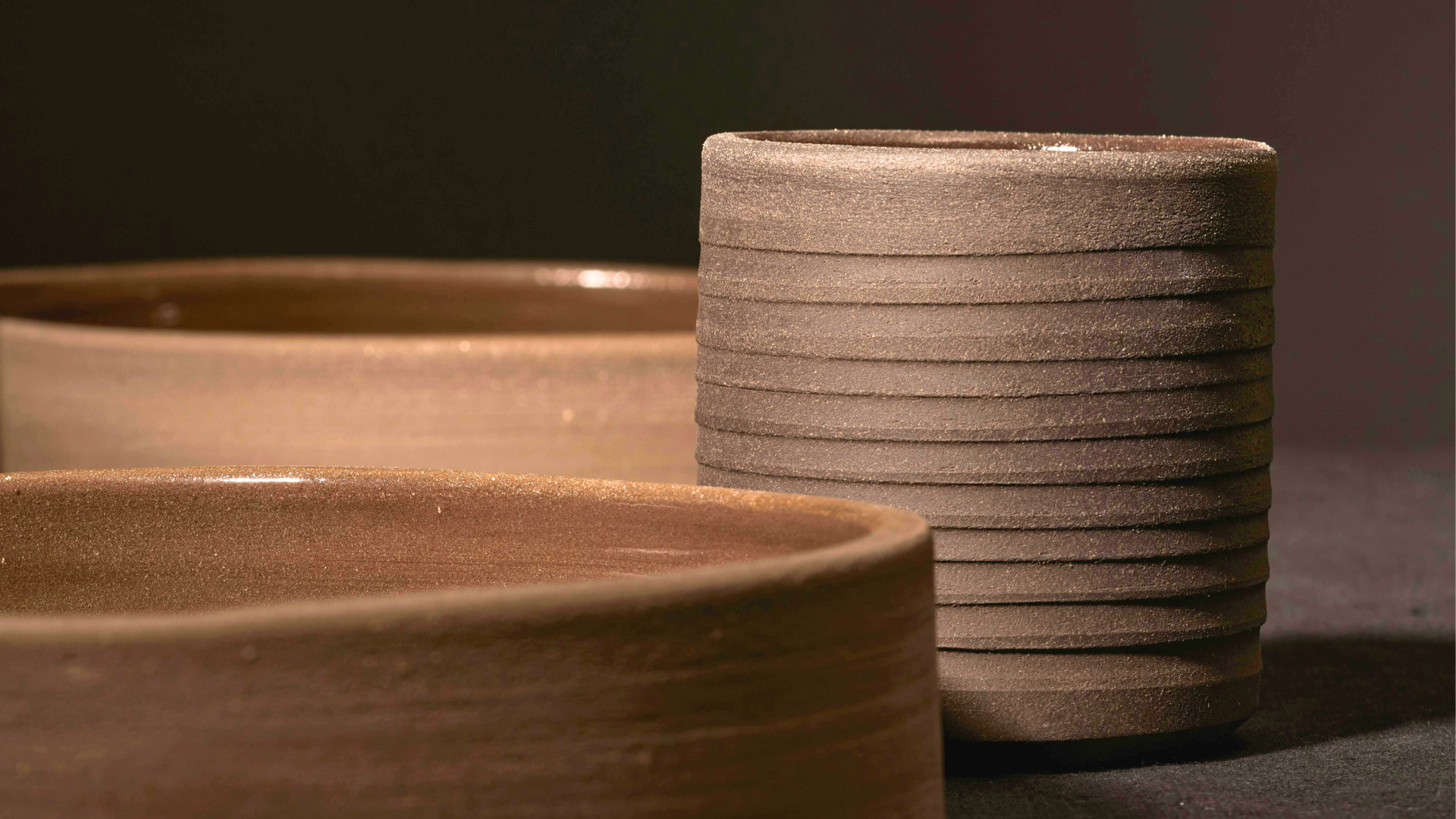 Close-up of handcrafted textured brown ceramic bowls and cup in a minimalist setting