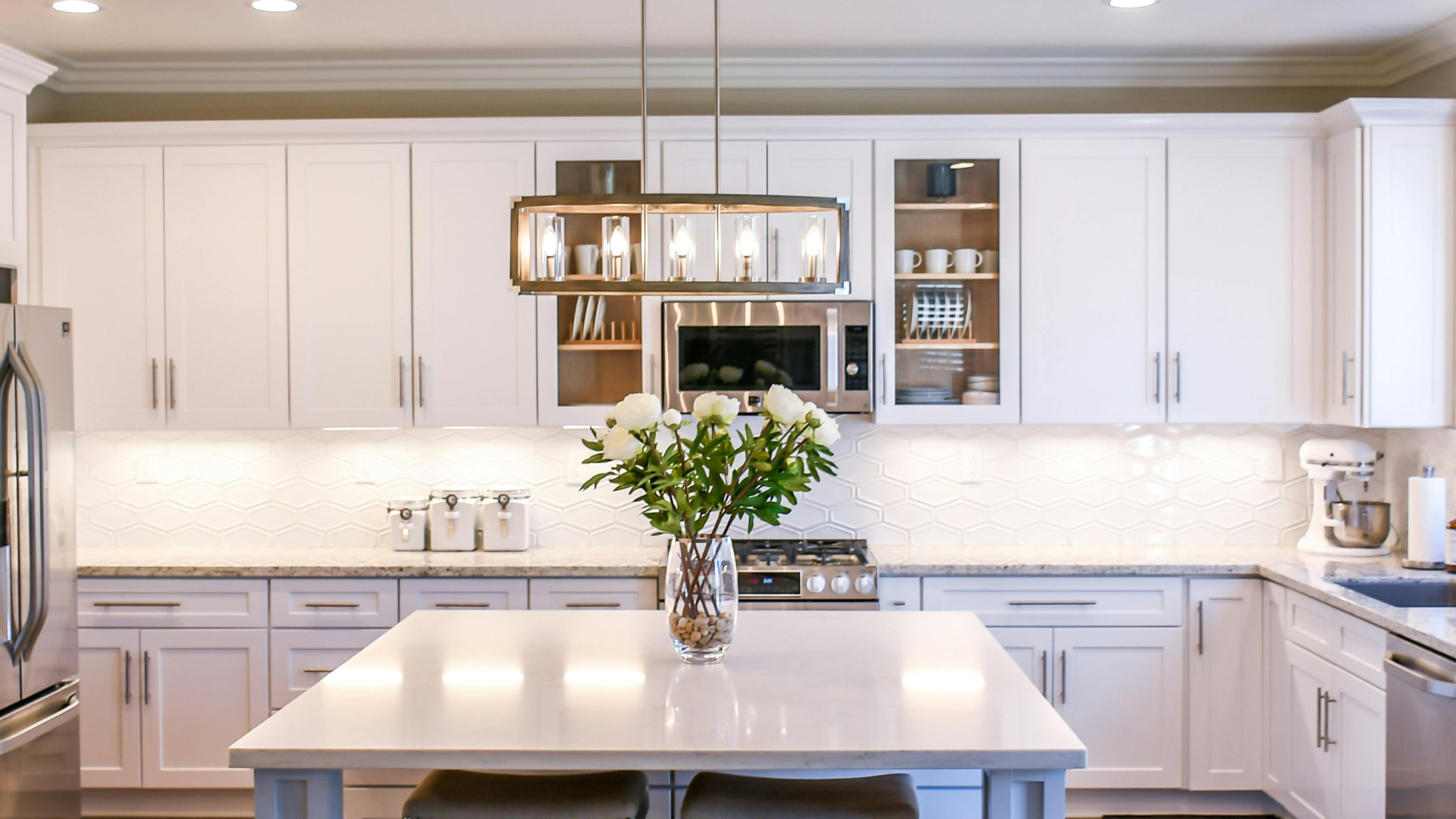 Bright white kitchen with flower arrangement on island and modern lighting fixture