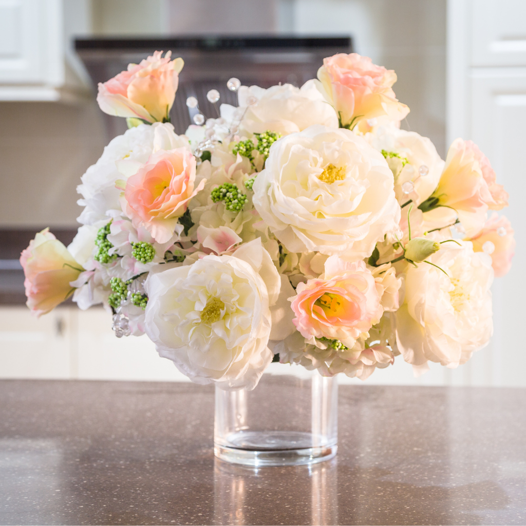 Soft pink and white roses in a clear glass vase on a kitchen counter