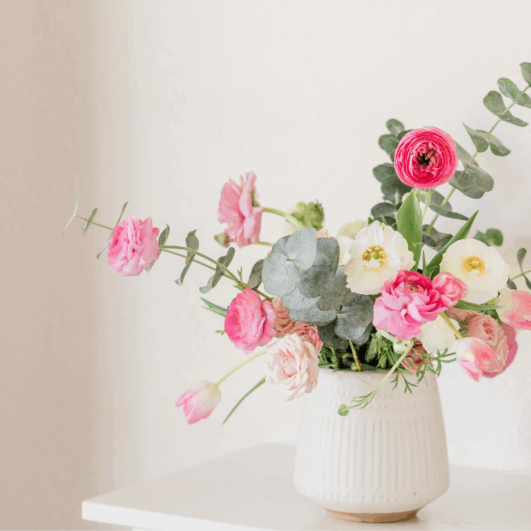 Pink and white ranunculus with eucalyptus in a white ceramic vase