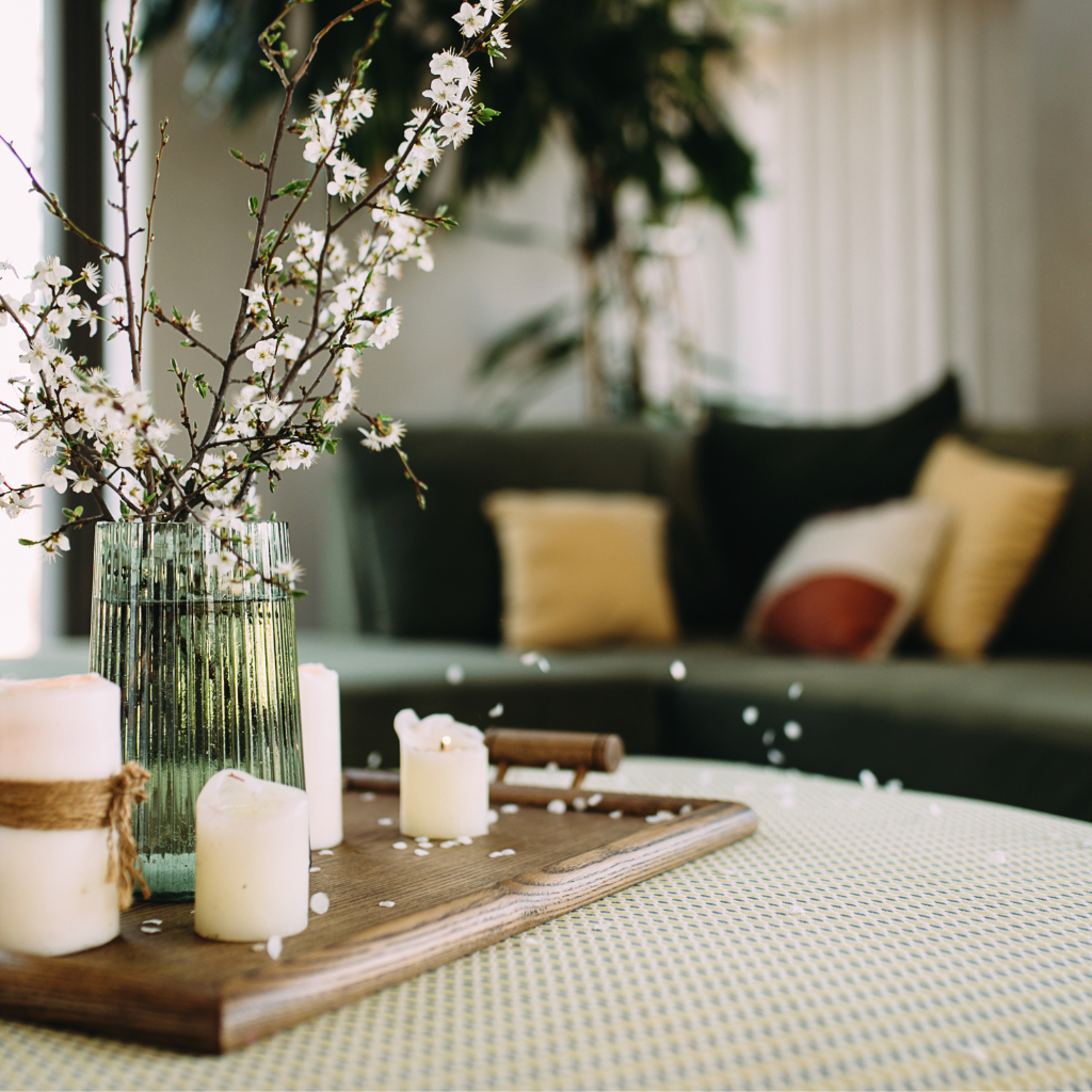 White spring blossoms in a green glass vase with candles on a wooden tray