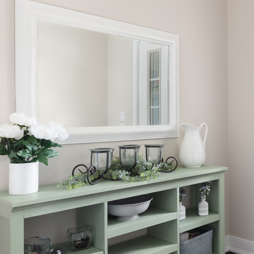 Green console table with white flowers, candles, and a mirror above