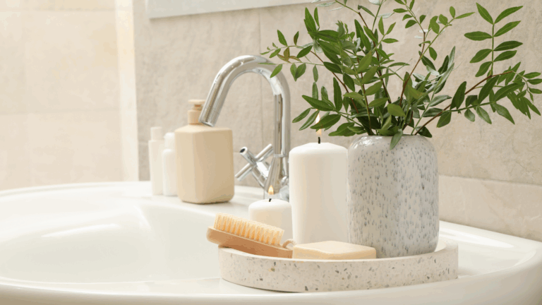 Bathroom sink with candles, soap, ceramic vase with greenery, body brush, and neutral-toned toiletries styled for a serene spa ambiance.