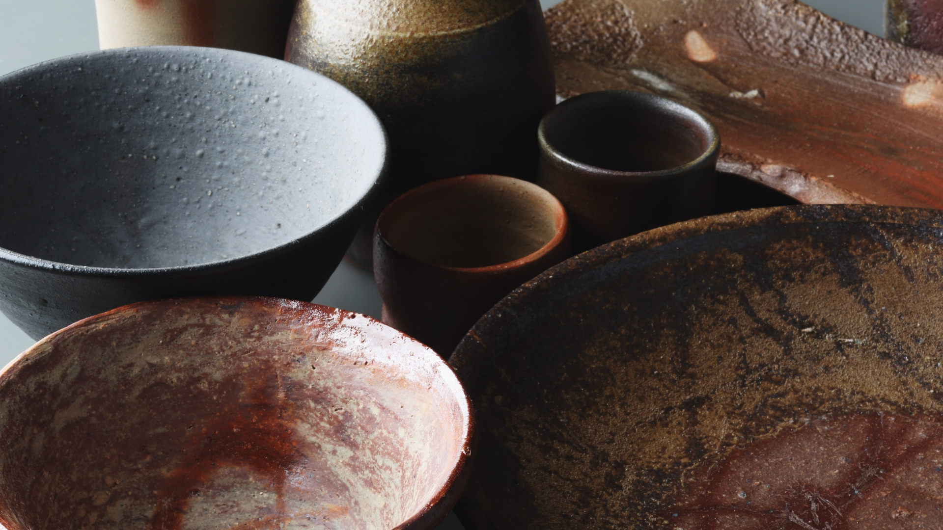 Collection of rustic textured ceramic bowls and cups in earthy tones