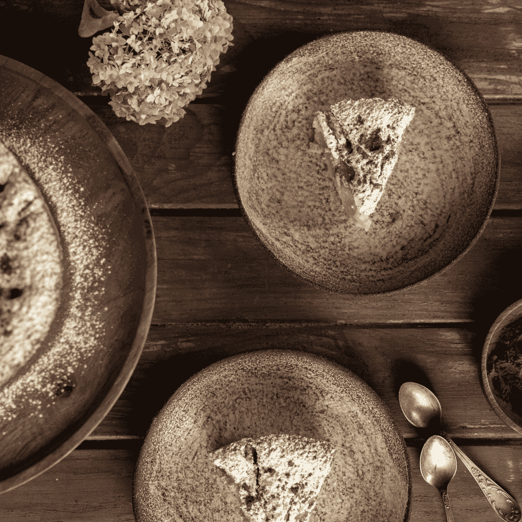 Rustic fall dessert setting featuring slices of powdered apple pie on ceramic plates, wooden table, silver spoons, and dried flowers.