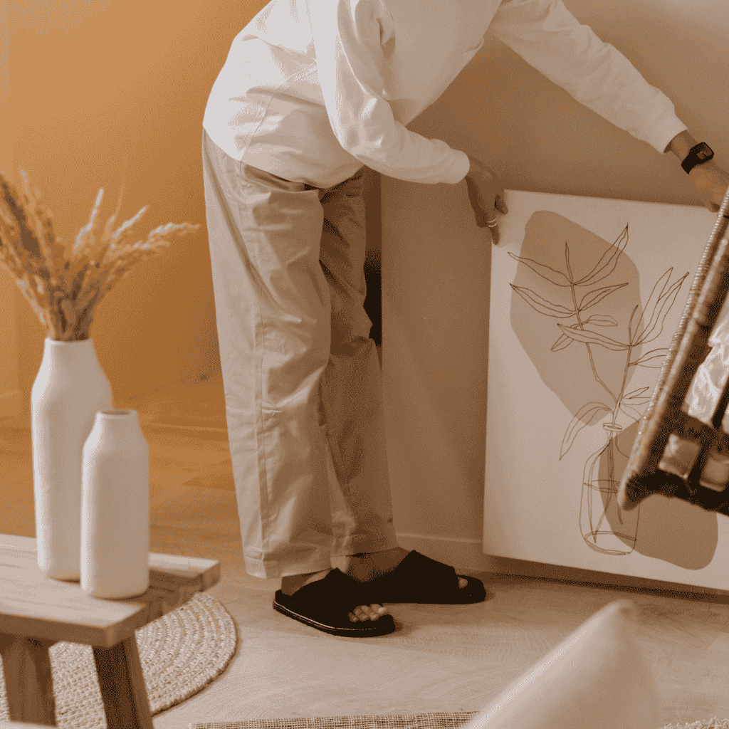 Person styling wall art in a cozy, neutral living space.