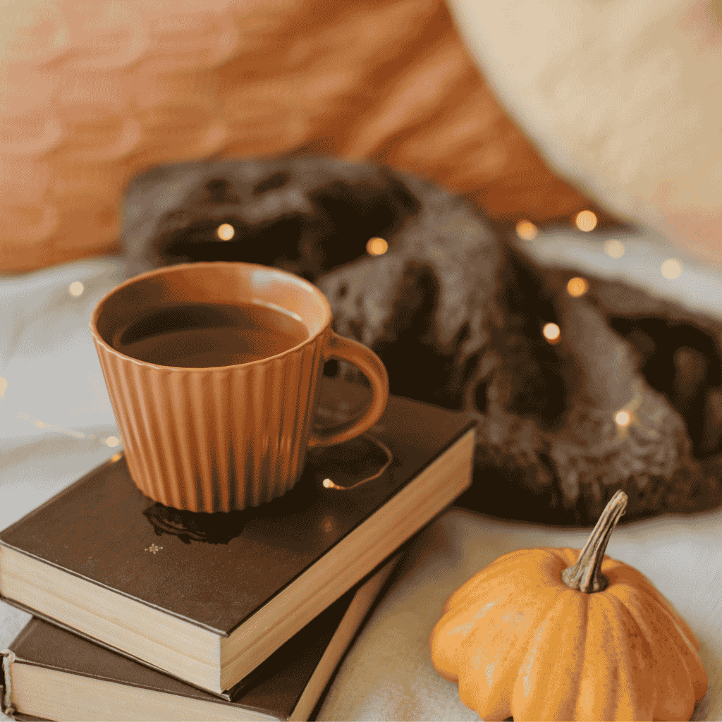 Warm drink in a brown cup on stacked books with a mini pumpkin beside it.