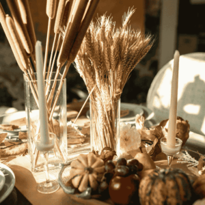 Rustic fall centerpiece with wheat stalks, pumpkins, and candles on a cozy dining table.