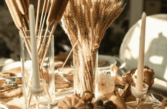 Rustic fall centerpiece with wheat stalks, pumpkins, and candles on a cozy dining table.