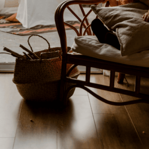 A cozy rattan chair beside a woven basket filled with sticks, resting on a polished wooden floor near a sunlit window — a perfect reflection of rattan, bamboo, and wood this fall.