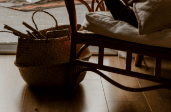 A cozy rattan chair beside a woven basket filled with sticks, resting on a polished wooden floor near a sunlit window — a perfect reflection of rattan, bamboo, and wood this fall.
