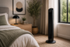 Black tower fan with digital display placed by the window in a warm minimalist bedroom with oak nightstand.