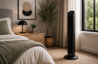 Black tower fan with digital display placed by the window in a warm minimalist bedroom with oak nightstand.