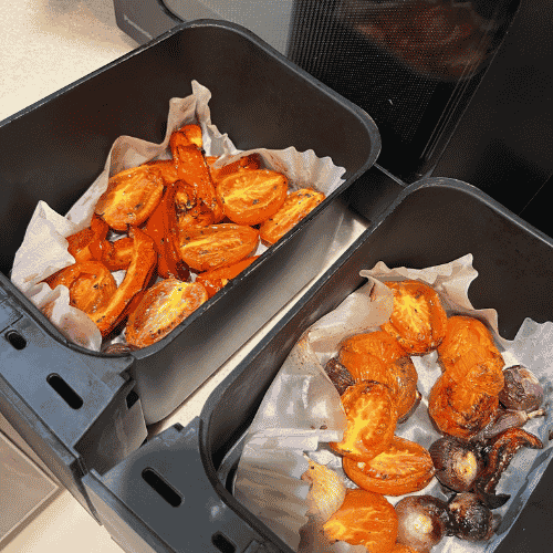 Roasted tomatoes, carrots, and onions in both Ninja Foodi DualZone baskets lined with paper for easy cleanup