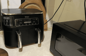 Ninja Foodi DualZone air fryer tucked into a small kitchen corner beside a microwave to save counter space.