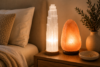 White selenite tower lamp and pink Himalayan salt lamp glowing side-by-side on a wood nightstand in a calm bedroom.